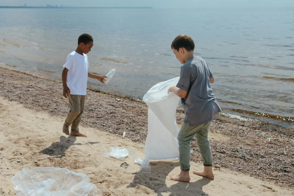 Two boys collect garbage at the beach, promoting volunteerism and environmental care.
